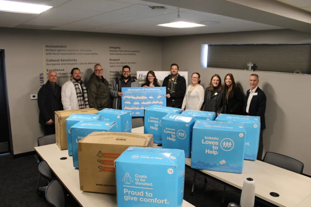 Subaru of Wichita donating boxes of coats. Assorted boxes laid out on a table with people standing behind the boxes.