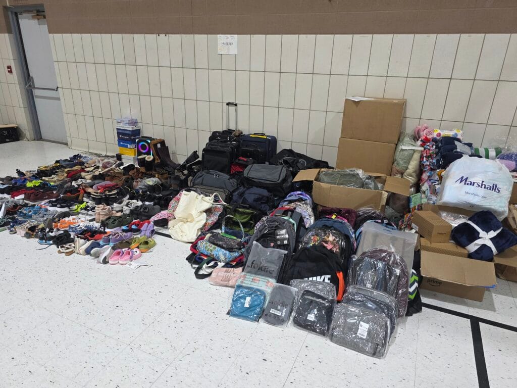 A large array of shoes, blankets, and bags are arranged on a gym floor
