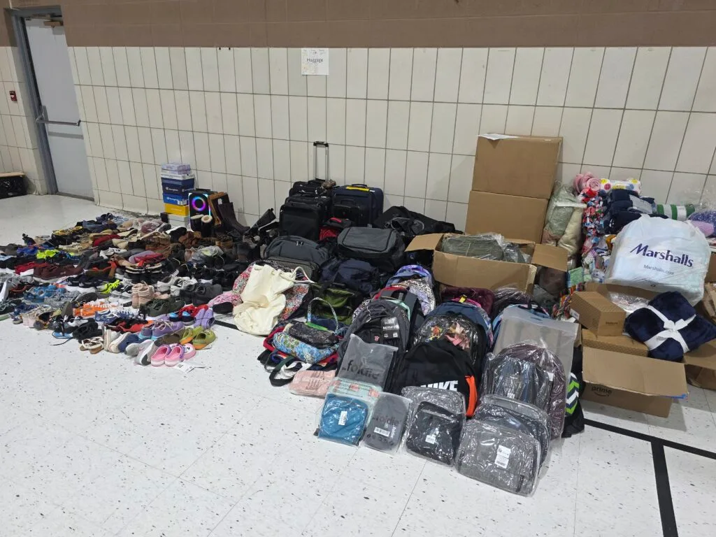 A large array of shoes, blankets, and bags are arranged on a gym floor