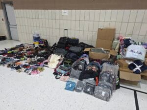 A large array of shoes, blankets, and bags are arranged on a gym floor