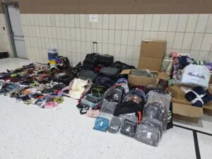 A large array of shoes, blankets, and bags are arranged on a gym floor