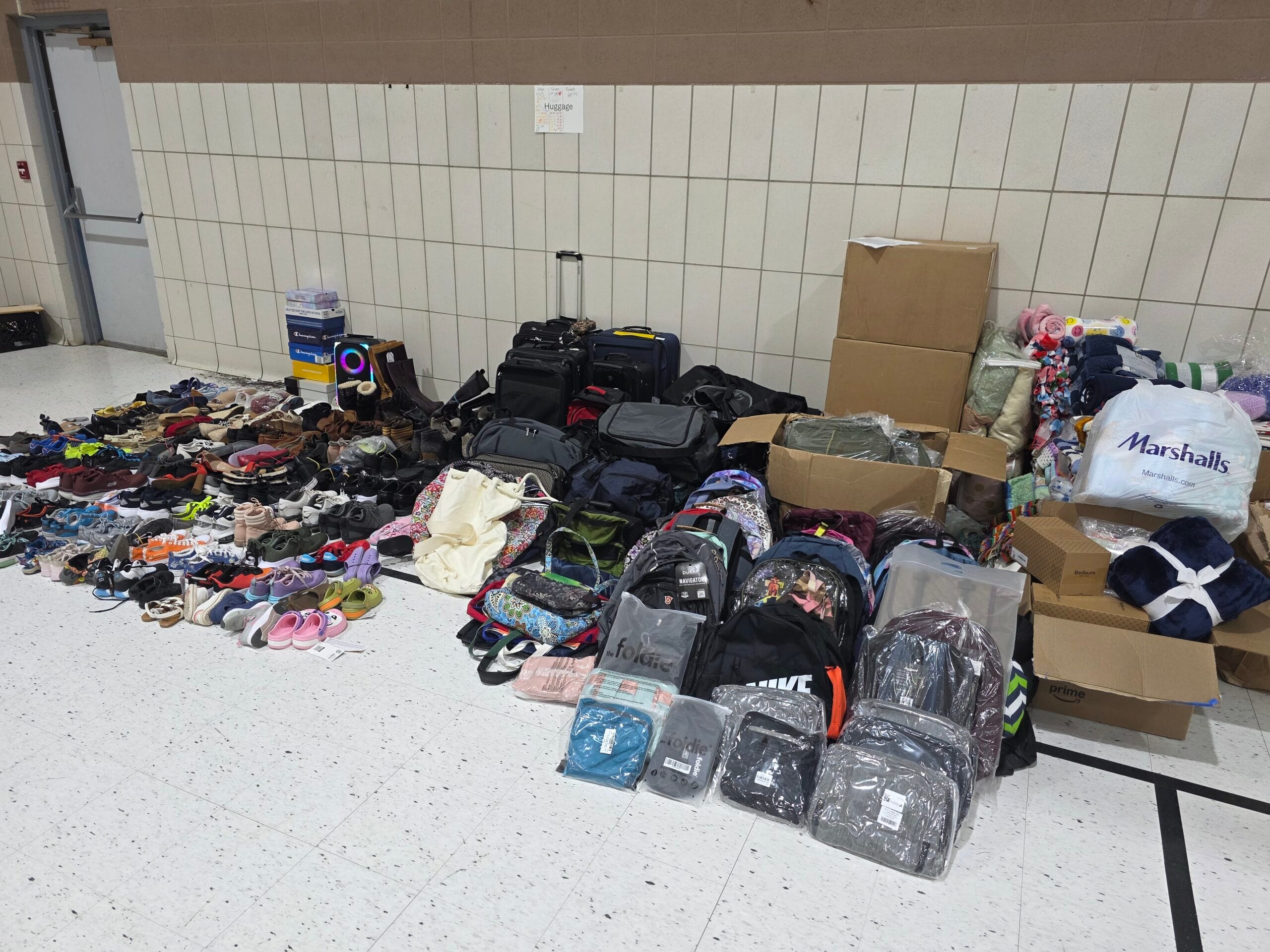 A large array of shoes, blankets, and bags are arranged on a gym floor