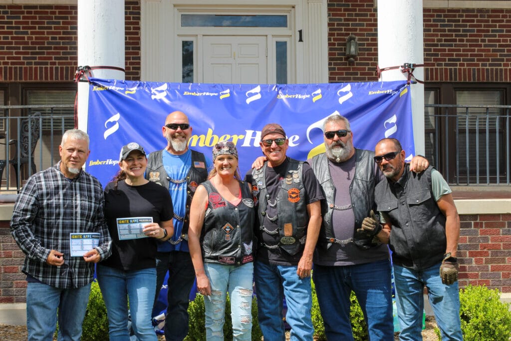 Poker run riders stand in front of the EmberHope banner at the Newton campus