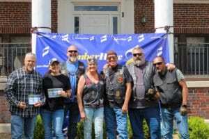 Poker run riders stand in front of the EmberHope banner at the Newton campus