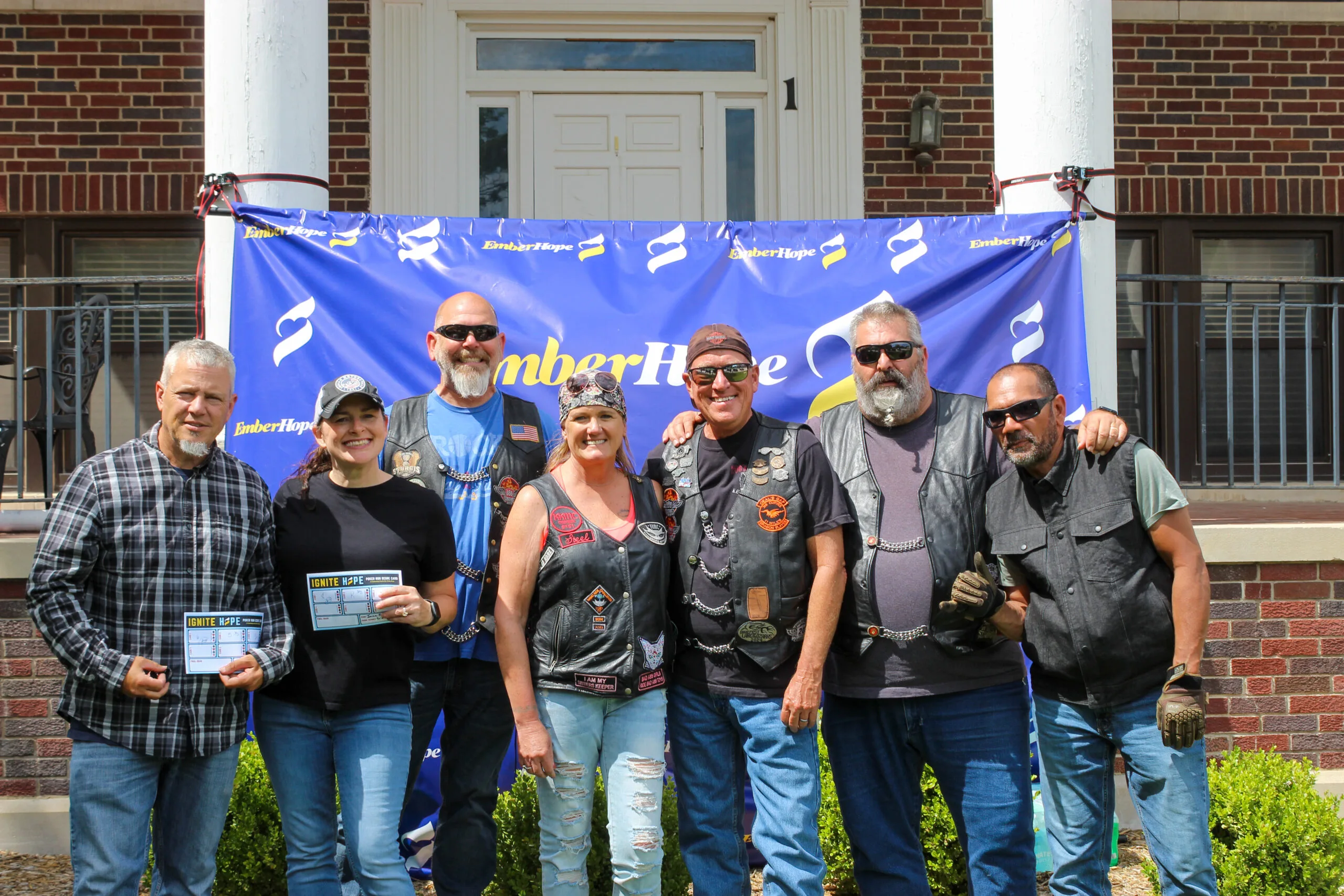 Poker run riders stand in front of the EmberHope banner at the Newton campus